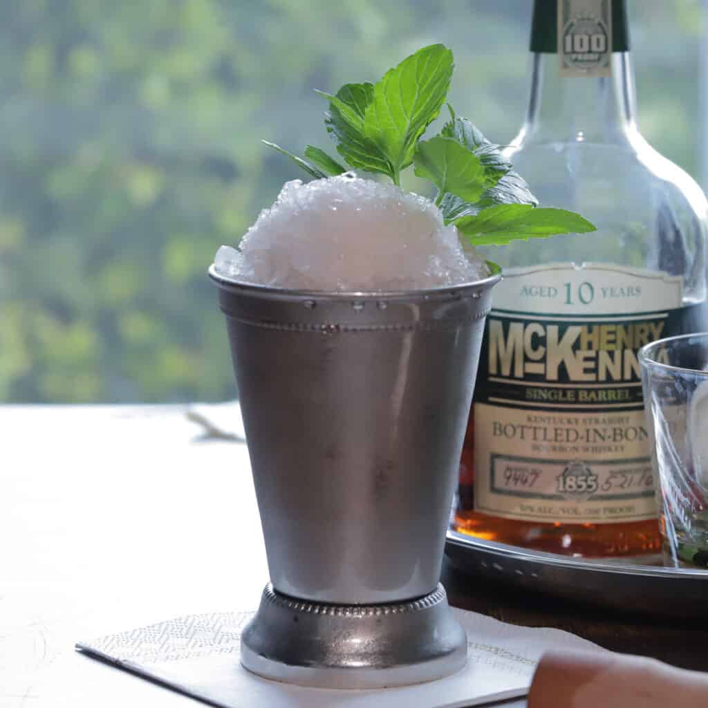 mint julep cocktail in a silver julep cup next to a bottle of McKenna bourbon